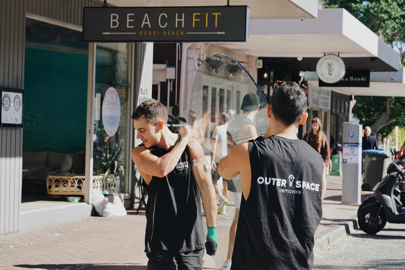 Two Outer Space movers carrying a glass table past the BeachFit studio in Bondi